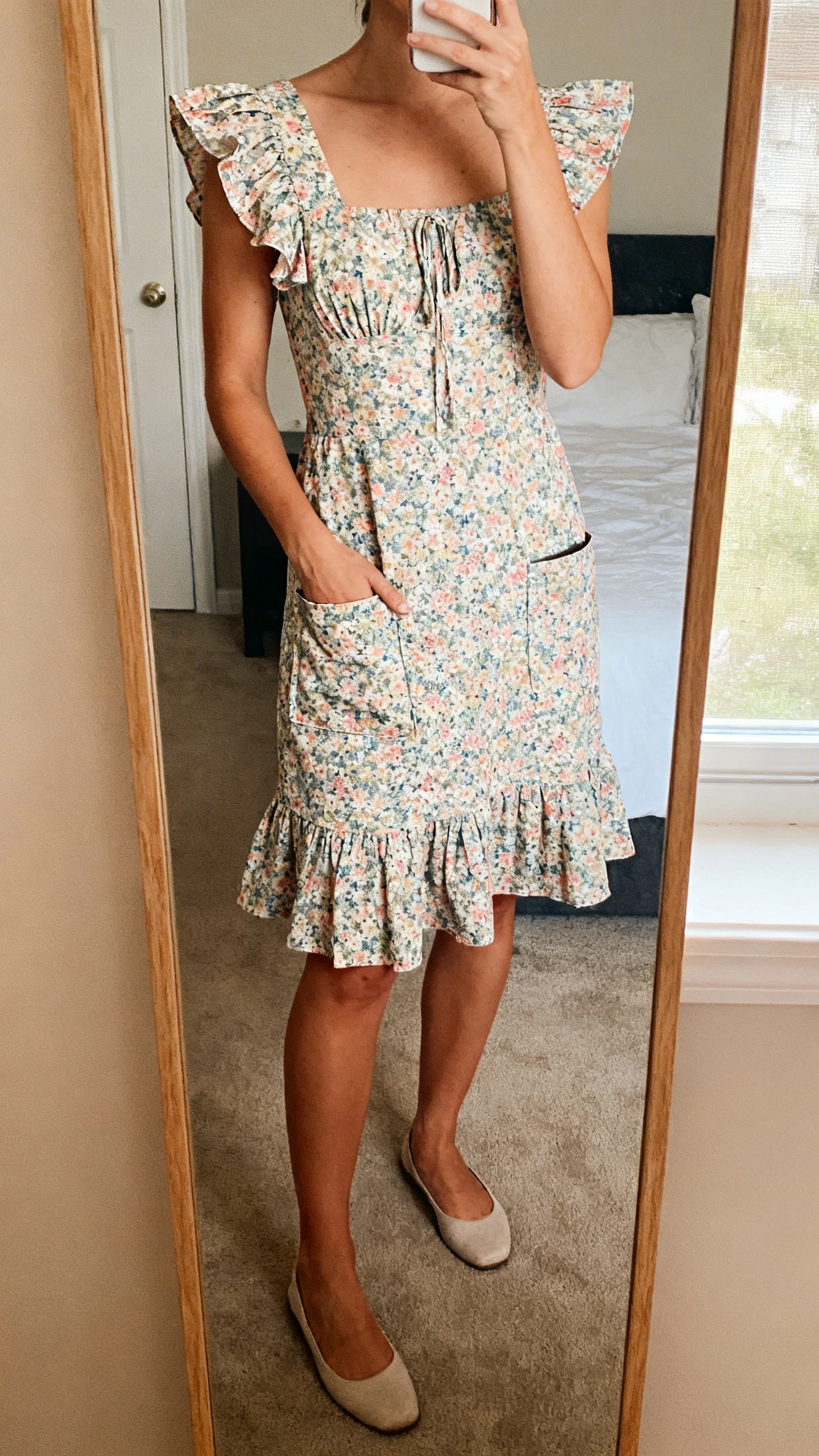 iPhone mirror selfie of a woman in a garden-party flutter dress with flutter sleeves and pockets, simple flats, face not visible, cropped at neck, bedroom mirror, natural window light, iPhone photo quality.