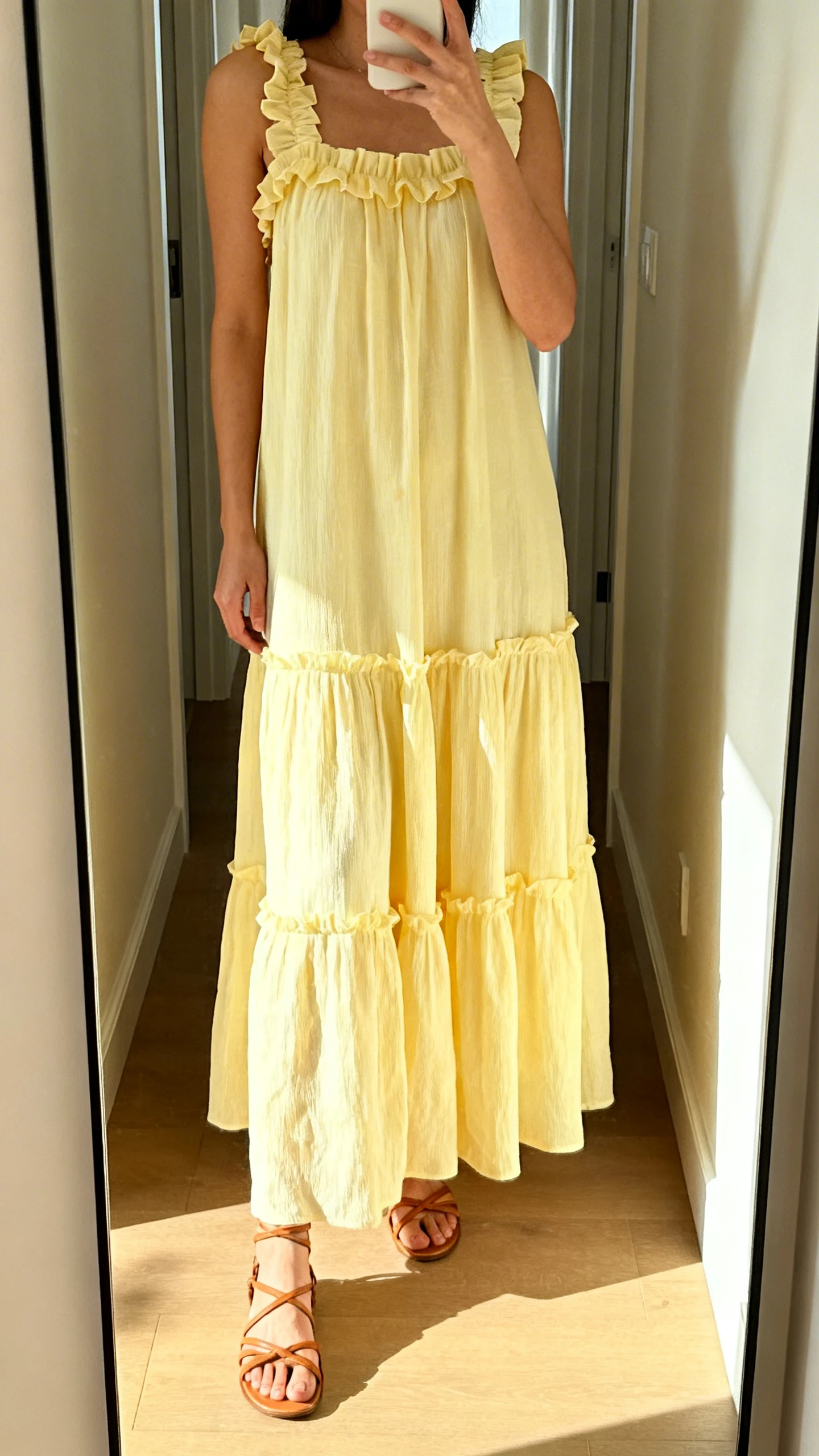 iPhone mirror selfie of a woman in a sunny-day tiered maxi dress with ruffle straps and strappy sandals, face not visible, cropped at shoulders, hallway mirror, bright morning light, iPhone photo quality.
