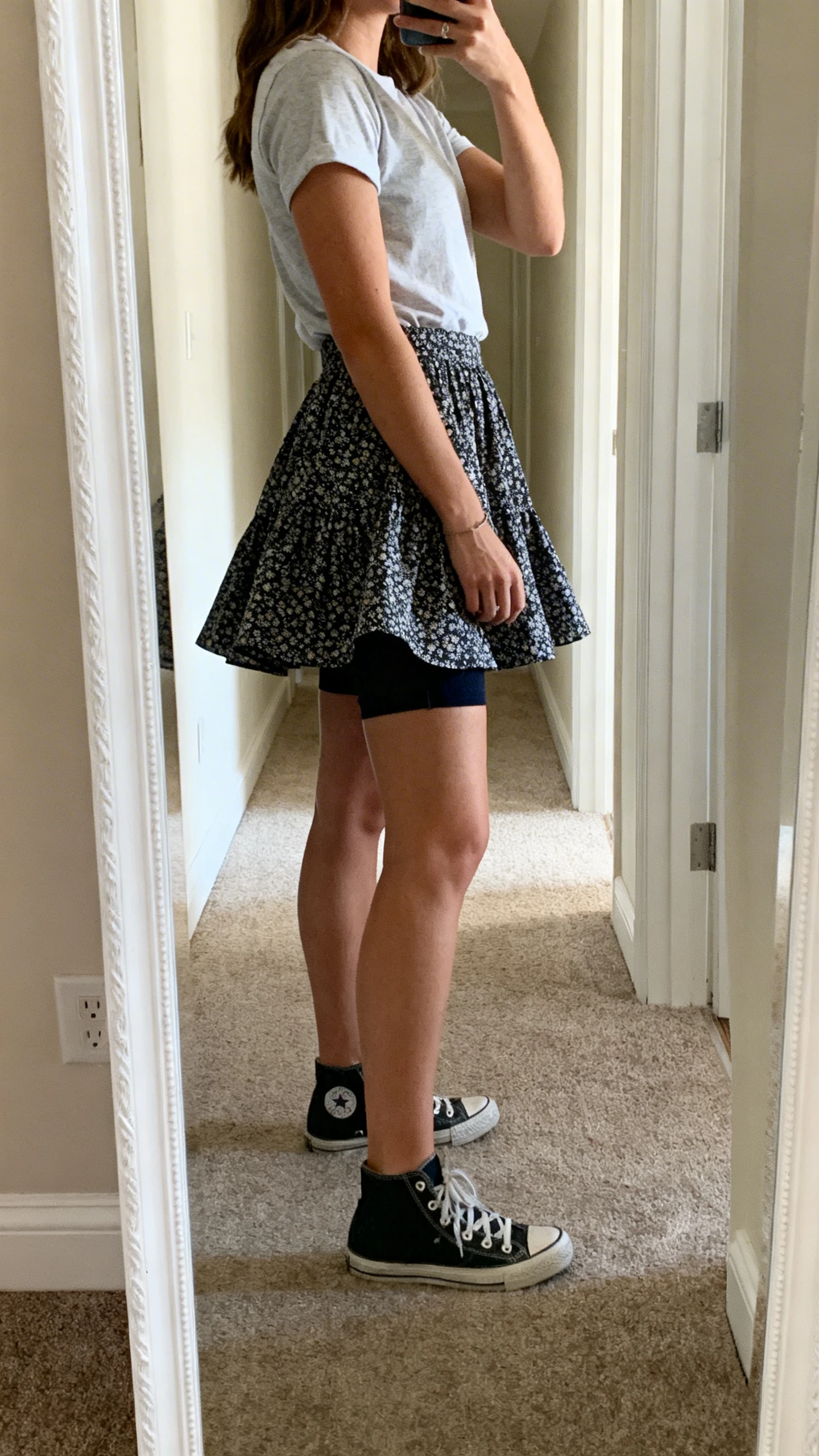 iPhone mirror selfie of a woman in a twirl-city circle skirt with hidden shorts, tucked-in tee, and sneakers, face not visible, side angle, full-length mirror in hallway, natural daylight, iPhone photo quality.