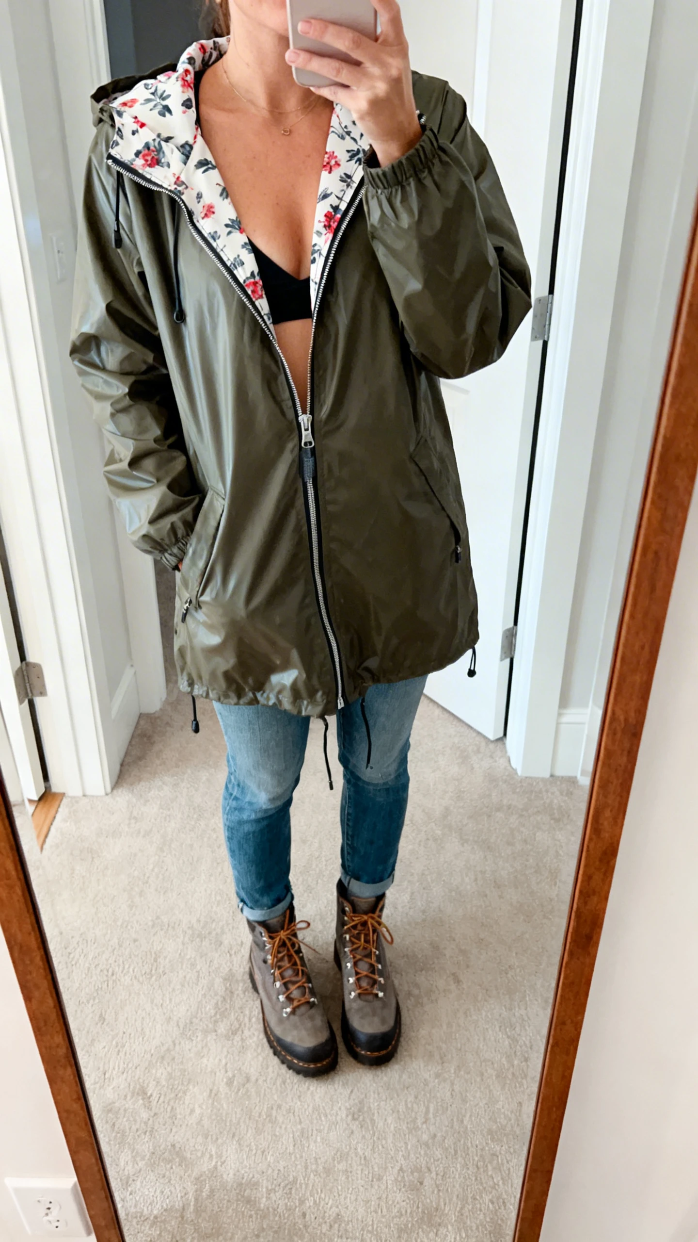 iPhone mirror selfie of a woman wearing a rain-dance anorak with a peekaboo printed lining, zipped halfway over jeans and lace-up boots, face not visible, cropped at shoulders, entryway mirror, natural light, iPhone photo quality.