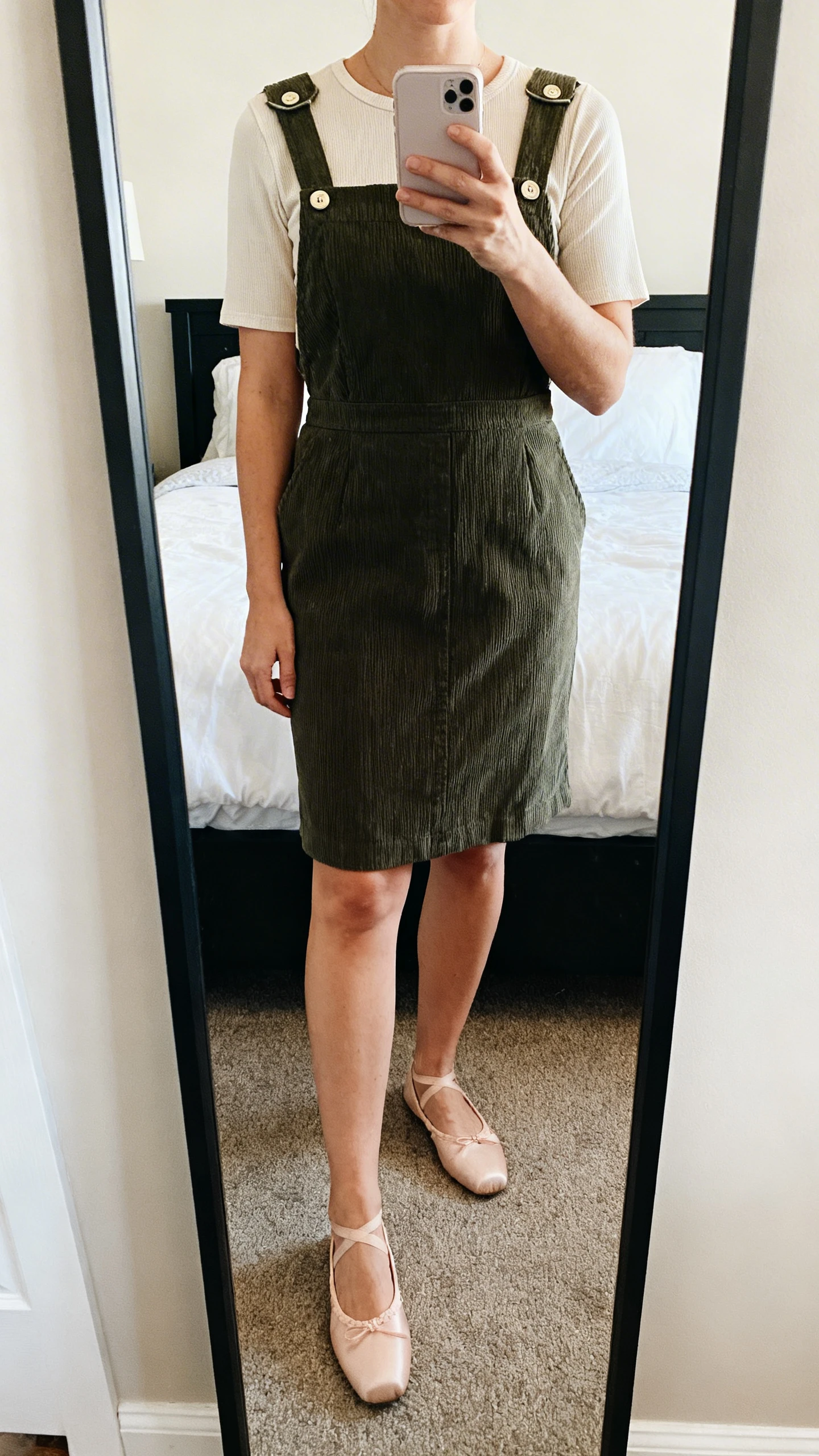 iPhone mirror selfie of a woman wearing a reversible pinafore with snap shoulders over a short-sleeve top, paired with ballet flats, face not visible, cropped at neck, bedroom mirror, natural light, iPhone photo quality.